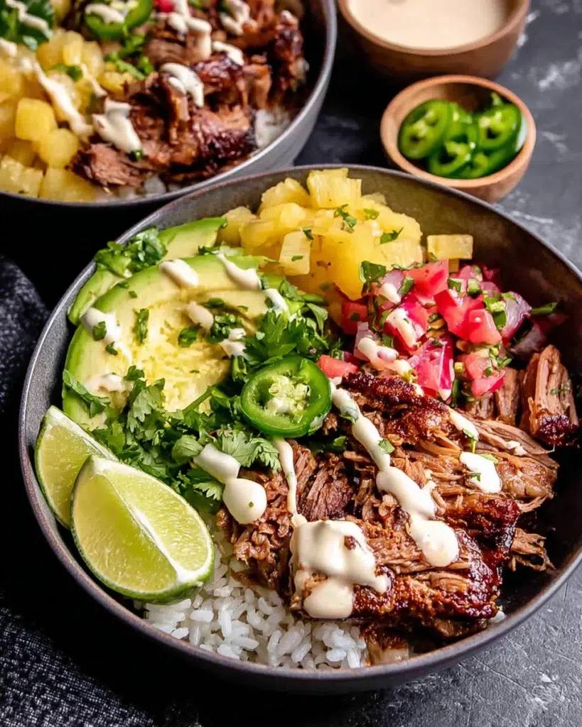 Crockpot Chipotle Pineapple Pot Roast Bowls with shredded beef, caramelized pineapple, avocado salsa, jalapeño, cilantro, rice, and creamy bang bang sauce served in a bowl.