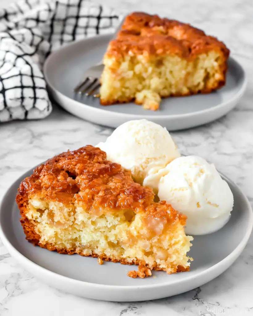 A warm slice of Dolly Parton's fruit cocktail cake with a golden crunchy top and soft fruity center, served on a white plate with a scoop of vanilla ice cream.