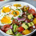 Workout Egg Avocado Salad served on a white marble counter, featuring jammy soft-boiled eggs with golden yolks, creamy avocado cubes, cherry tomatoes, sliced red onion, fresh cilantro, and red pepper flakes in a colorful homemade salad.